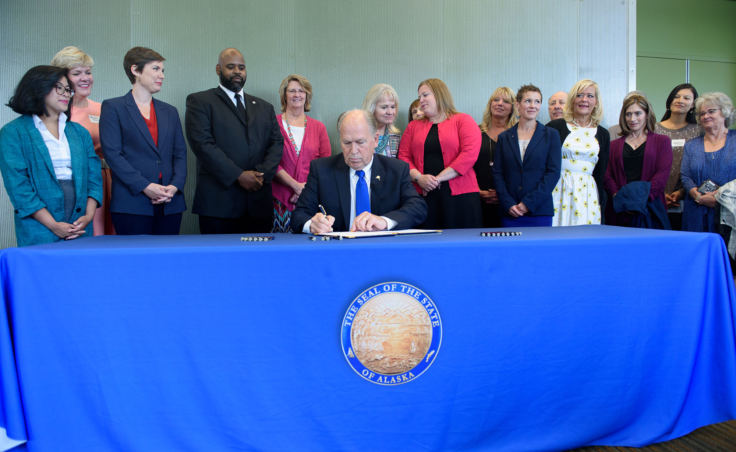 Gov. Bill Walker signs Senate Bill 105 into law during an Anchorage Chamber of Commerce luncheon at the Dena'ina center in Anchorage on Aug. 6, 2018. The bill promotes competition for health care services by requiring providers to post prices for their most common health care services. Also pictured are Rep. Ivy Sponholz, third from the left, Sen. David Wilson, fourth from left, first lady Donna Walker directly behind the governor, and Rep. Geran Tarr to her left.