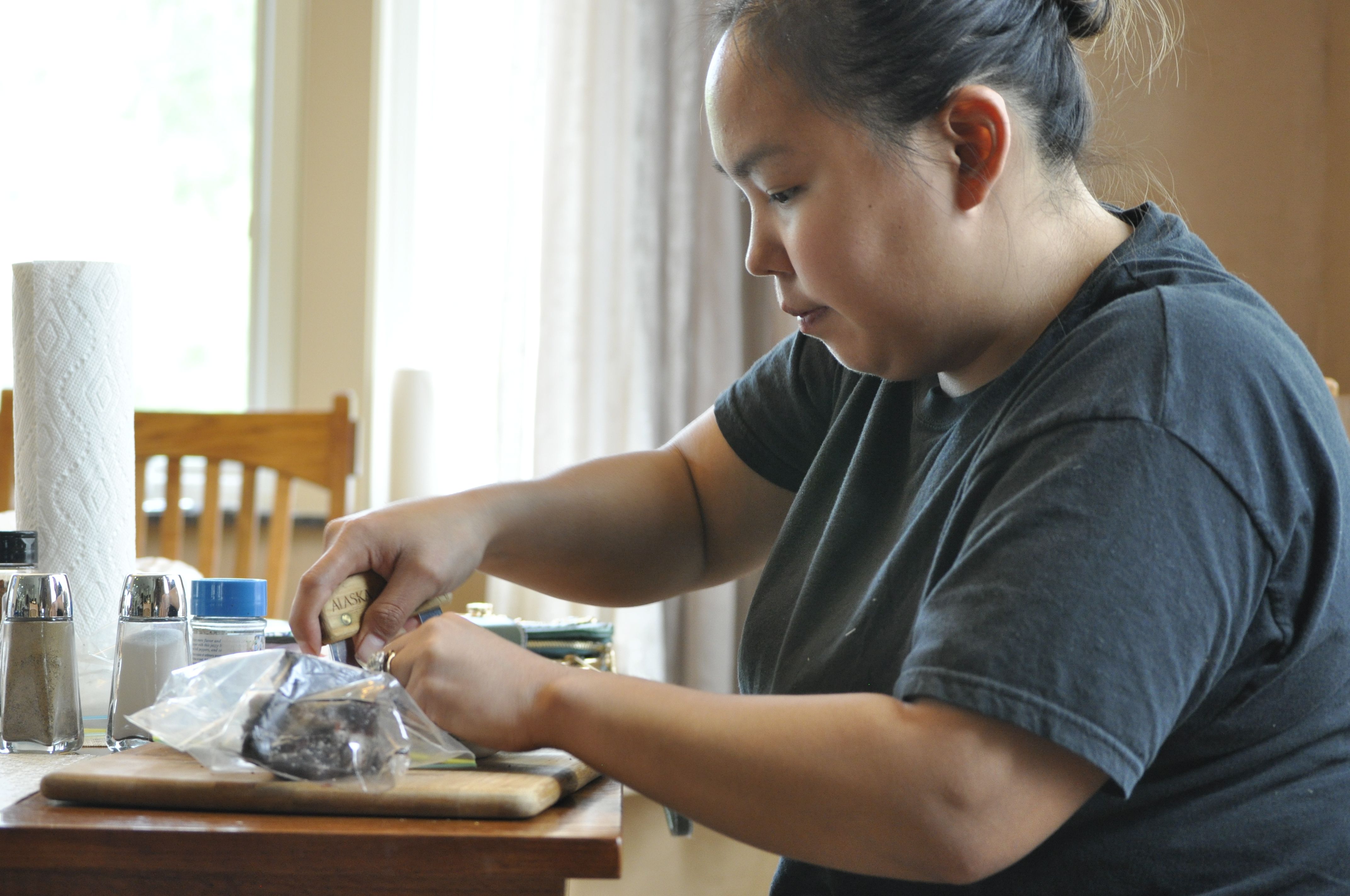 Alesha Tangman uses an ulu to cut up pieces of bowhead whale meat at her aunt and uncle’s kitchen table in Wasilla. She uses Kunniak’s spice mixtures on everything from salads to Maktak. (Photo by Erin McKinstry/Alaska Public Media)