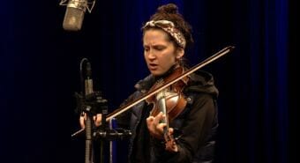 A picture of a woman playing a violin and singing into a microphone.
