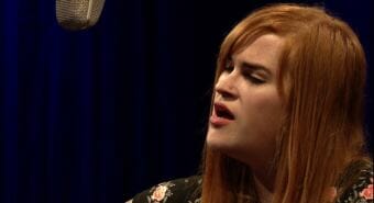 Image of woman singing into microphone in television studio. Video still of Dara Rilatos performing a Red Carpet Concert at KTOO during the 2018 Alaska Folk Festival.
