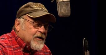 Picture of man singing into microphone. Longtime Juneau musician Mike Truax performs his song "It's Me" for a Red Carpet Concert during the 2018 Alaska Folk Festival at KTOO in Juneau. (Screen capture image from video https://www.youtube.com/embed/vpuxQATosZ0 )