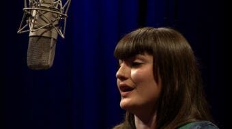 A picture of a woman singing into a microphone. Video still of Alaska songwriter recording a Red Carpet Concert video performance @360 during the 2018 Alaska Folk Festival at KTOO Public Media in Juneau.