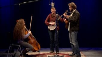 An image of a woman playing cello, a woman playing banjo and a man playing guitar on a stage around a microphone. A video still of the Anchorage folk group String of Lights performing a Red Carpet Concert at KTOO Public Media during the 2018 Alaska Folk Festival.