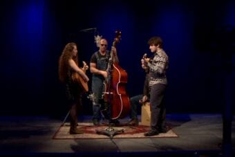 A band plays around a microphone in a television studio. A still image of The Tanana Rafters of Anchorage performing a Red Carpet Concert at KTOO during the 2018 Alaska Folk Festival.