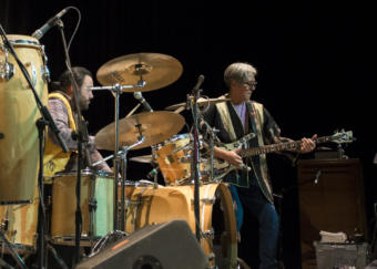 A man plays bass while another man plays on a drum kit. Tlingit glass artist and founding member of the band Khu.éex' Preston Singletary plays bass at Centennial Hall with Sitka percussionist Ed Littlefield on drums, Monday, January 28, 2019. (Photo by Annie Bartholomew/KTOO)