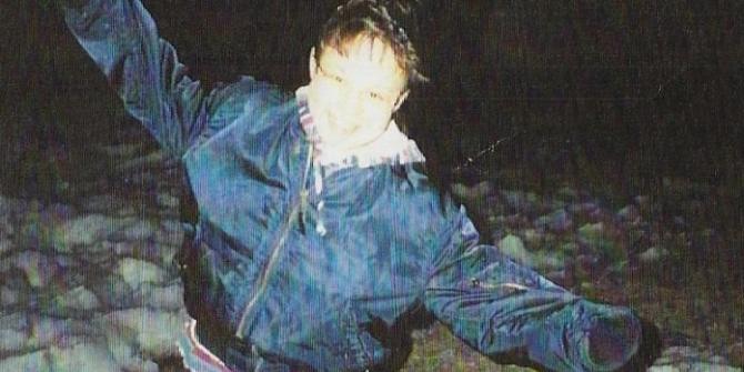 A night photo of a young woman in a blue jacket smiling and playfully holding her arms out from her sides