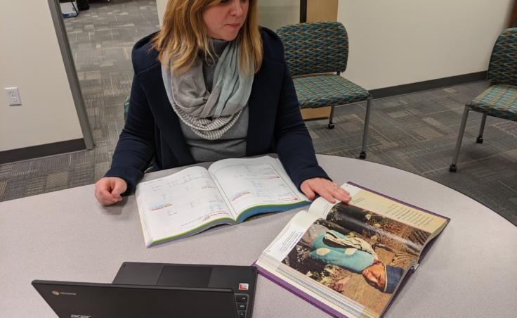 Jennifer Knutson, the senior director of teaching and learning for the Anchorage School District, shows some textbooks and a district-issue Chromebook that students have access to on March 13, 2020. She says that there will need to be a combination of traditional and e-learning opportunities for students during school closure. (Photo by Mayowa Aina/Alaska Public Media)