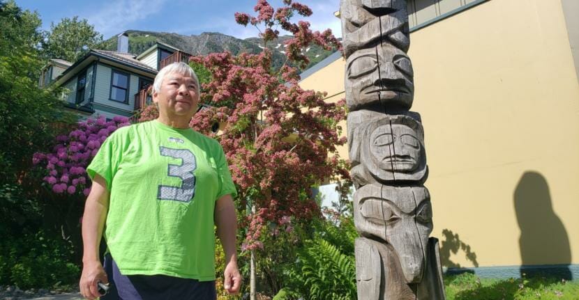 Photographer Brian Wallace poses for a picture next to a totem pole his father, Amos Wallace, carved outside the Juneau-Douglas City Museum in Juneau on June 12, 2020.