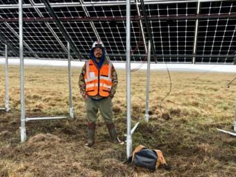 A man in an orange vest stands in front of a solar panel array