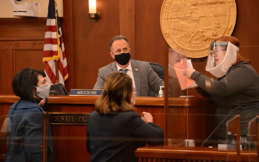 Alaska Senate Secretary Liz Clark (right) holds a copy of the Alaska Legislature's uniform rules on Wednesday, March 10, 2021 as she talks to Sen. Lora Reinbold, R-Eagle River (center) while Senate President Peter Micciche, R-Soldotna and Senate Majority Leader Shelley Hughes, R-Palmer, look on. Reinbold was excluded from most spaces in the Alaska State Capitol until she follows the Legislature's anti-COVID policies. (James Brooks/Anchorage Daily News via AP, Pool)
