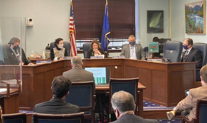 Sen. Lora Reinbold, R-Eagle River, at center, briefly lowers his face shield to ask Attorney General Treg Taylor a question during his confirmation hearing on March 24, 2021, in the Alaska State Capitol in Juneau, Alaska. Taylor, seated with his back to the camera, had asked her to clarify a question. Senators Robert Myers, R-North Pole; Shelley Hughes, R-Palmer; Mike Shower, R-Wasilla; and Jesse Kiehl, D-Juneau, also are seated at the committee table. (Photo by Andrew Kitchenman/KTOO and Alaska Public Media)