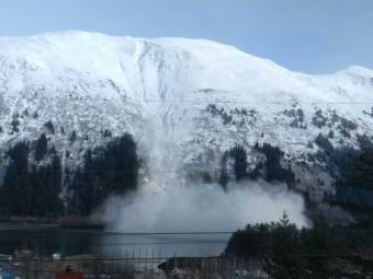 An avalanche cascading down a steep, coastal mountain into the water