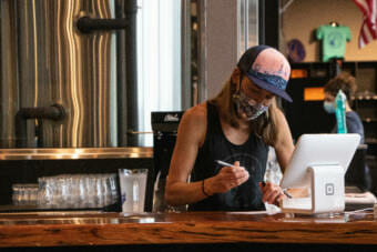 Sara Stekoll works behind the counter June 25 at Forbidden Peak Brewery in Juneau, Alaska. She is a co-owner of the brewery and asked the City and Borough of Juneau to host a vaccine clinic there. (Photo by Lyndsey Brollini/KTOO)