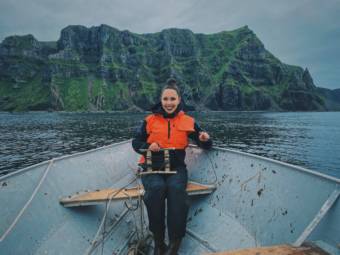 A woman in the bow of a boat on the water with green cliffs in the background