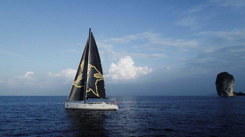 A sailboat with a dog's head on its sail, sailing in open water with a rock pillar in the background