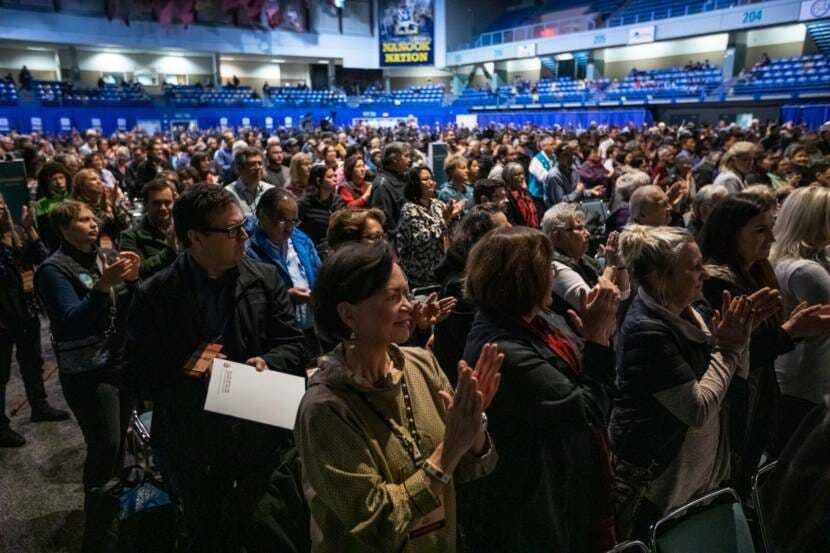 An audience, all standing, filling the floor of an arena
