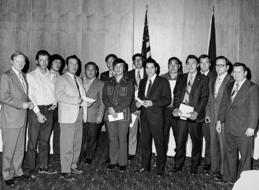 A black-and-white photo of a group of 14 men posing together inside a hotel