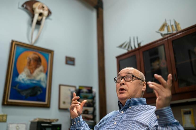 A man sitting in an office, gesturing with both hands as he speaks.