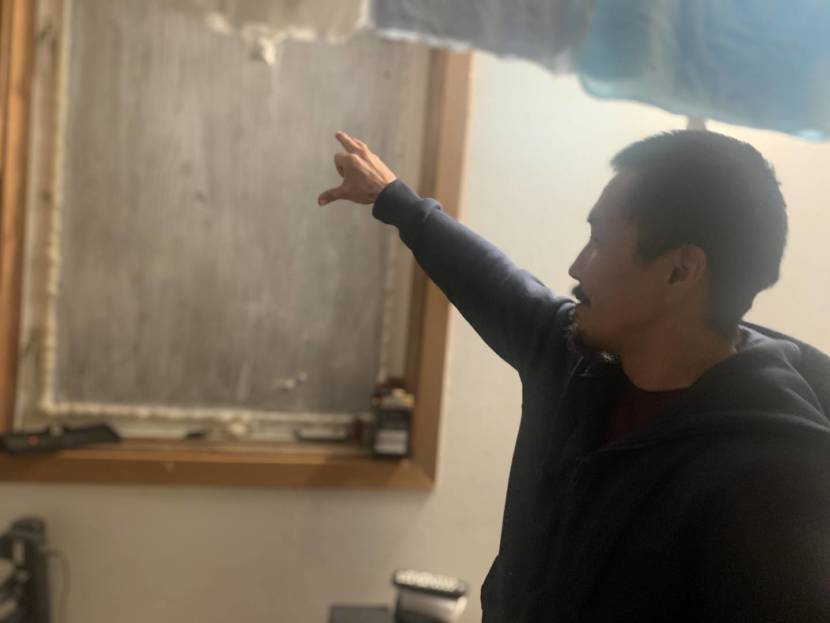 A man inside a house points at a boarded-up window