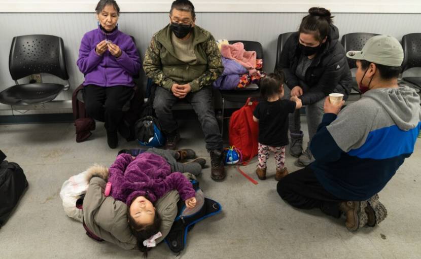 A child sleep on a pile of coats in front of two adults sitting in plastic airport chairs.