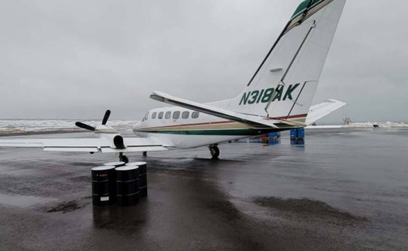 A twin engine plane sitting on a wet runway next to four fuel drums