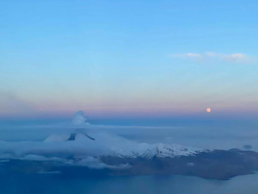 A volcano with a small plume above it, seen from an airplane at twilight