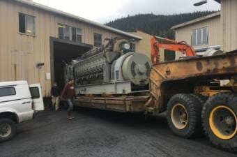 A large electric generator is backed into an open garage door on the back of a flatbed truck.