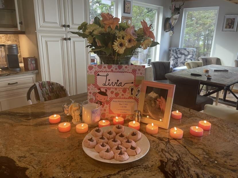 A plate of cookies, lit candles, a card, brightly colored flowers and a photo of a baby are arranged on a table as a shrine in memory of pregnancy loss. 