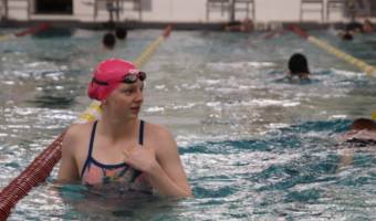 Lydia Jacoby standing in a pool with kids swimming laps in the background