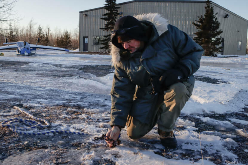 A man crouches on the ground near an aircraft hanger.