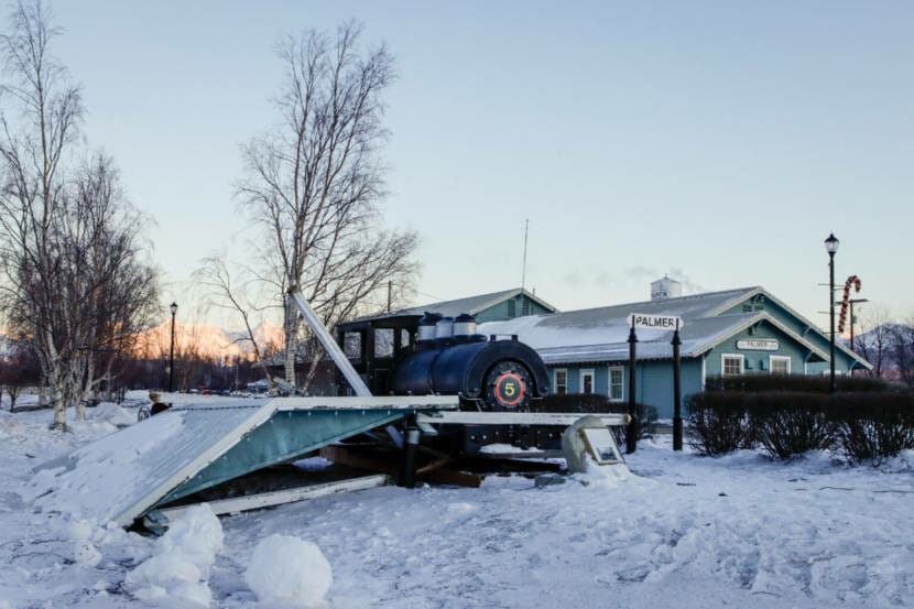 A small park pavilion lies collapsed in front of an old steam engine