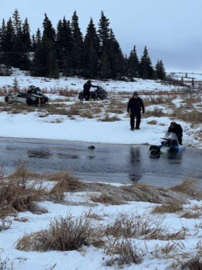 Several people looking at a snowmachine half-sunk in a frozen river
