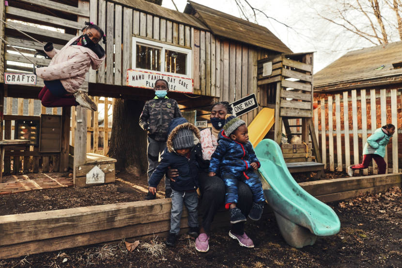 A woman holding two children on her lap on a playground while other kids play around them