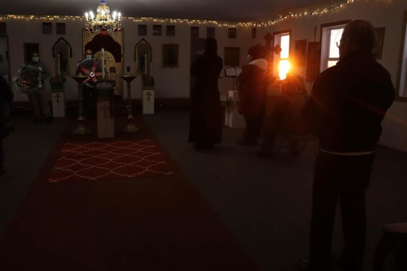People standing inside a dark church with the rising sun appearing in one window