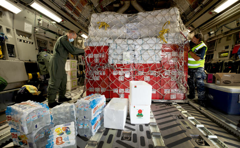 Two men on either side of a pallet of supplies in the hold of a cargo plane