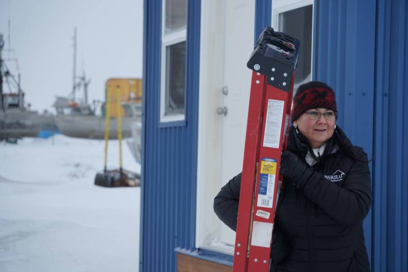 A woman carrying a stepladder outside in the snow