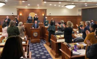 A man stands at a lectern at the front of a courtroom as people around him applaud