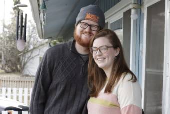 A young couple standing outside their front door