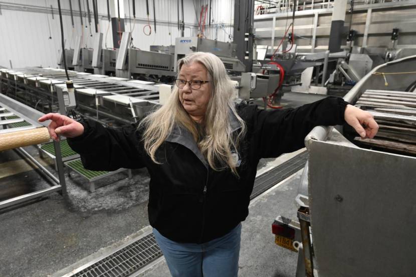 A woman in an otherwise empty seafood plant points at something outside the frame