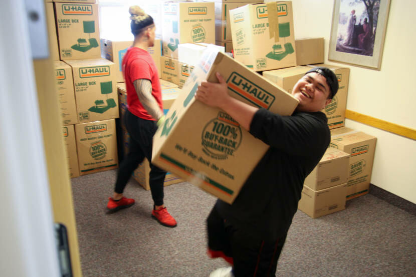 A young man carrying a large box that he can barely get his arms around.