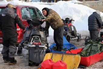 A young man standing by a snowmachine parked next to a car