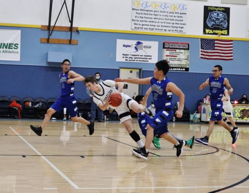 A basketball player falling while another player reaches out to steal the ball from him.
