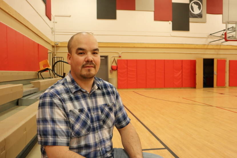 A portrait of a man in a plaid shirt sitting by a basketball court