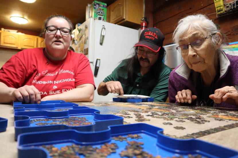 Three people sitting around a table, doing a crossword puzzle together.