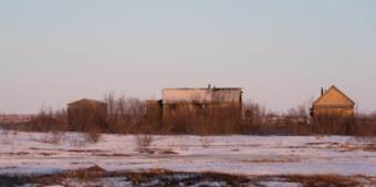 A burned-out home stands between two smaller structures on a snowy, tundra landscape