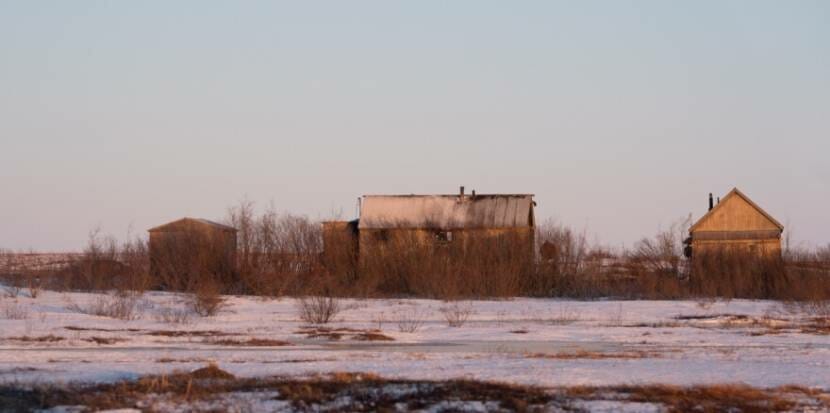 A burned-out home stands between two smaller structures on a snowy, tundra landscape