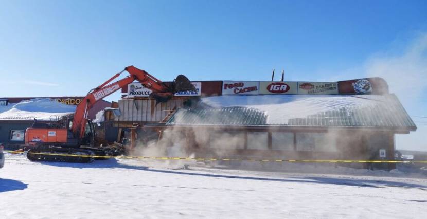 An excavator beginning to demolish the front of a grocery store