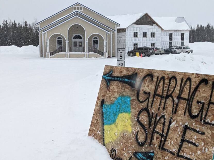 A garage sale sign with a Ukrainian flag painted on it, outside a church