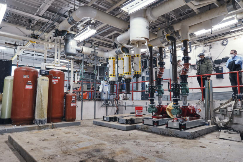 Three people stand in a boiler room