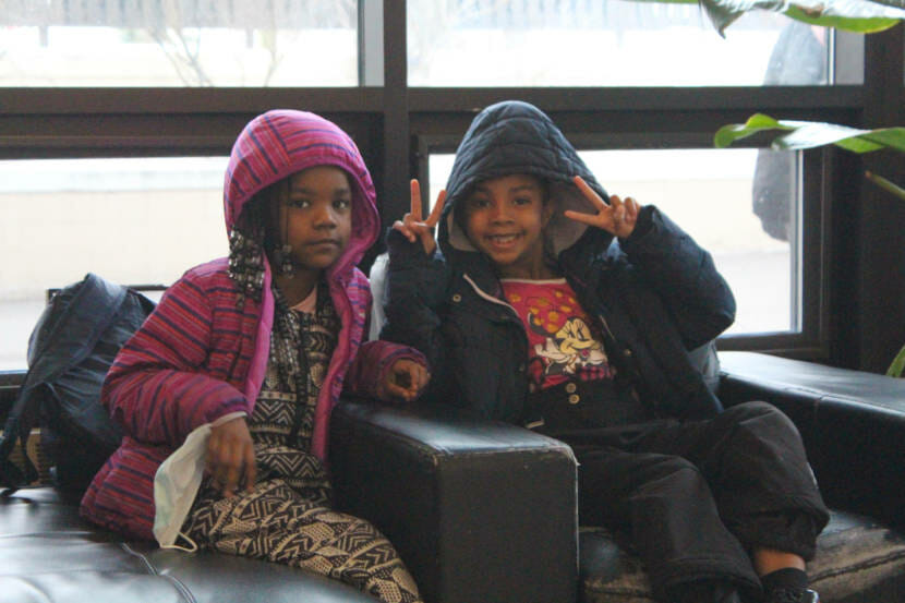Two children, dressed for school, smile for a photo in a hotel lobby